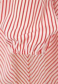 Czerwono-biała w paski tkanina, miękka w dotyku, z detalem ściąganym w mankiecie rękawa oraz ukośnymi paskami tworzącymi wzór w zygzak.