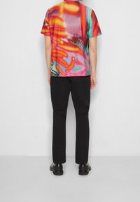 Chemise à manches courtes avec un imprimé abstrait multicolore vibrant ; tissu lisse ; associée à un pantalon noir et des chaussures noires.