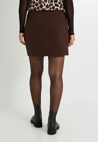 Mini falda de pana marrón con un diseño recto, que cuenta con dos bolsillos traseros. Combinada con botas negras hasta el tobillo y medias transparentes.