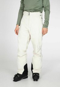 Witte skibroek met een gladde textuur, voorzien van een hoge taille en twee voorknoopjes. Gecombineerd met zwarte skibotten en een aansluitend groene top.