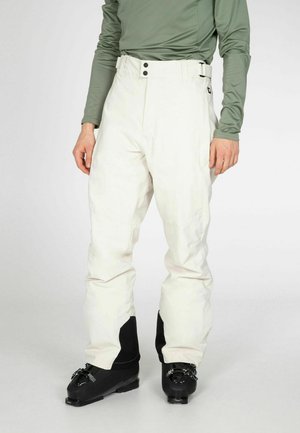 Witte skibroek met een gladde textuur, voorzien van een hoge taille en twee voorknoopjes. Gecombineerd met zwarte skibotten en een aansluitend groene top.