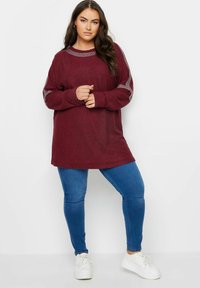 Burgundy oversized sweatshirt med nitar på ärmarna, ihopparat med blå skinny jeans och vita sneakers. Smoother textur, avslappnad design.
