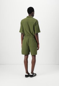 Combinaison verte à manches courtes avec taille élastique et poche arrière. Fabriquée en tissu texturé, elle présente un col et une coupe décontractée.