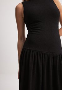 Must mustriga kleit, millel on sobiv lõige ja tekstuuriga kangas ning laienev, volditud seelik. Kaelus on ümmargune, ilma nähtavate kinnitusteta.