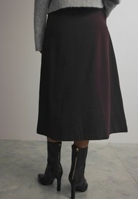 Zwarte midi rok met een gladde textuur, met een uitlopende silhouette, gecombineerd met zwarte hoge hakken met een ritssluiting aan de achterkant.