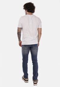 T-shirt bianco a maniche corte abbinato a jeans in denim blu scuro. I jeans presentano un aspetto leggermente usurato e l'outfit è completato da sneakers nere e bianche.