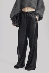Black leather wide-leg pants with a smooth texture and an elastic waistband, paired with a cropped gray fuzzy sweater and a black clutch.