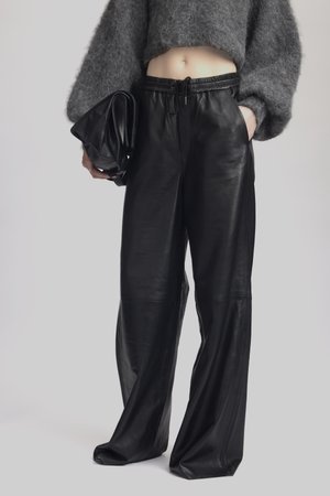 Black leather wide-leg pants with a smooth texture and an elastic waistband, paired with a cropped gray fuzzy sweater and a black clutch.