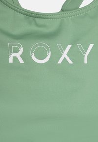 Mintgrüner Stoff mit einer glatten Textur zeigt den Markennamen "ROXY" in weißen, fettgedruckten Buchstaben in der Mitte.