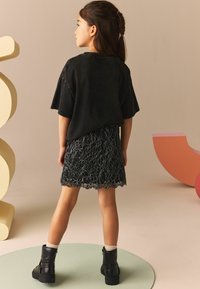 Sort oversized T-shirt kombinert med en sort spissløs skjørt, med en bølget kant. Båret med sorte ankelstøvler og kremfargede sokker.