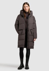 Puberová bunda v tmavošedej farbe s kapucňou, zipsovými vreckami a priliehavým strihom. Má hladkú textúru a elastické manžety.