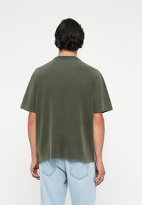 Olijfgroene T-shirt met korte mouwen van een zachte stof, met een losse pasvorm en ronde hals, gecombineerd met lichtblauwe jeans.