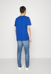 Camiseta azul de algodón con cuello redondo y mangas cortas, combinada con vaqueros azul claro y zapatillas blancas. Diseño simple y casual.