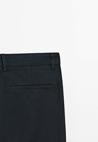 Pantaloni in lino neri con una texture liscia, vita tailored e una singola tasca posteriore con un'apertura orizzontale discreta.