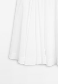 Jupe blanche en A fabriquée en tissu léger, avec des plis et un ourlet qui tombe au-dessus du genou, avec une texture lisse et douce.