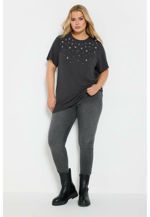 T-shirt grigio a maniche corte con motivo floreale in rilievo sul davanti, abbinato a jeans skinny grigio scuro e stivaletti neri.