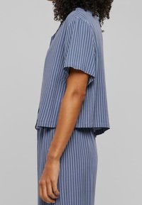 Top de mezcla de algodón en azul marino con rayas verticales blancas, mangas cortas, corte relajado y un dobladillo curvado. Diseñado con un cuello clásico.