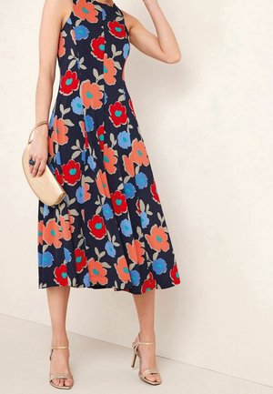 Granatowa sukienka midi bez rękawów z dużymi czerwonymi, pomarańczowymi i niebieskimi kwiatowymi wzorami, zestawiona ze złotymi szpilkami i beżową kopertówką.