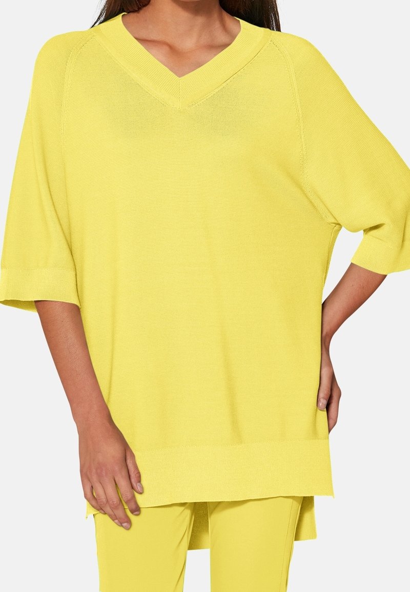 Žlutý volnější pletený top s výstřihem do V, krátkými rukávy a rovným lemem. Má texturovaný povrch a uvolněný střih.
