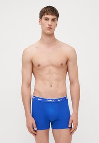 Kék pamut bokszernadrág, szoros illeszkedéssel, fehér rugalmas derékpánttal, amelyen vastag betűkkel szerepel a "NIKE" felirat.