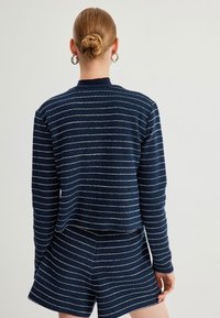 Navyblau gestreifter Strickpullover mit weißen Akzenten, runder Ausschnitt und langen Ärmeln, kombiniert mit passenden Shorts.
