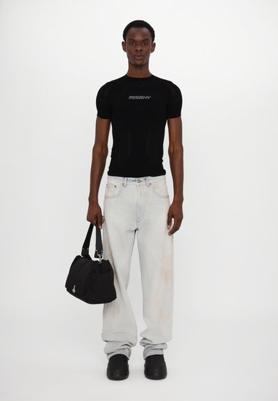 Maglietta nera aderente in maglia con rete traspirante, jeans baggy azzurri, borsa a tracolla nera e scarpe slip-on nere chunky.