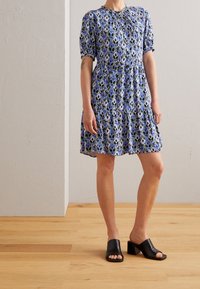 Vestido corto de manga corta con estampado azul, escote redondo, cintura ajustada y falda acampanada, combinado con mules negros de punta abierta.
