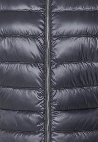 Námořnicky modrý péřový kabát s prošívaným designem, se soutěžním uzávěrem ze slitin. Hladká textura a zakulacené prošívané segmenty.