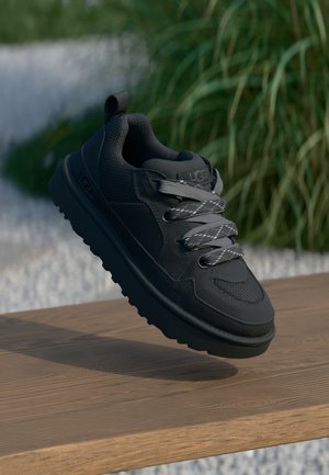 Black sneaker with textured mesh upper and smooth accents. Features gray laces and rubber sole with traction pattern. Floating above wooden surface.