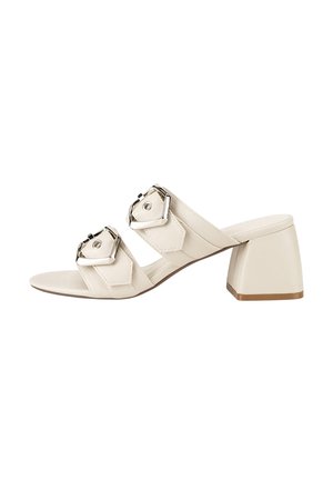 Kremowy sandał typu mule na otwartym palcu, z dwoma szerokimi paskami ozdobionymi dużymi srebrnymi klamrami oraz szerokim, średniej wysokości słupkowym obcasem.