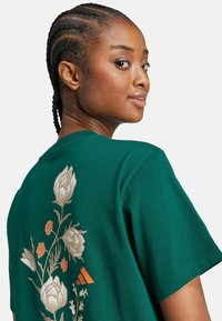 Camiseta de algodón verde con un diseño floral en dorado y naranja en la parte posterior. Mangas cortas y cuello redondo.