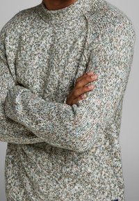 Gestrickter Pullover mit meliertem Muster in Grautönen, Creme und Braun. Rippstrickbündchen am Kragen und an den Ärmelabschlüssen, mit entspanntem Sitz.