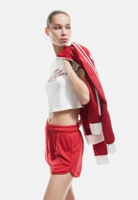 Rode sportjack met witte accenten, gecombineerd met een witte cropped top met tekst, en bijpassende rode shorts met een elastische tailleband.