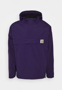 Lilla hættejakke lavet af vandafvisende stof, med en halv-lynlås foran, justerbare manchetter og logo-patch på brystet.