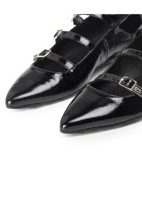 Zapatos planos de charol negro con punta afilada y dos correas decorativas con hebillas en tono dorado. Textura suave y brillante en toda su superficie.