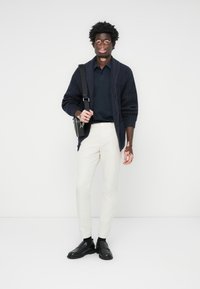 Mornarska pletena cardigan preko tamnog polo majice, bež uskih hlača i crnih cipela. Crna torba je bačena preko ramena.