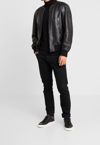 Svart läderbomberjacka, ribbade manschetter och nederkant, kombinerad med en svart polotröja och svarta jeans, avslutad med svarta sneakers.