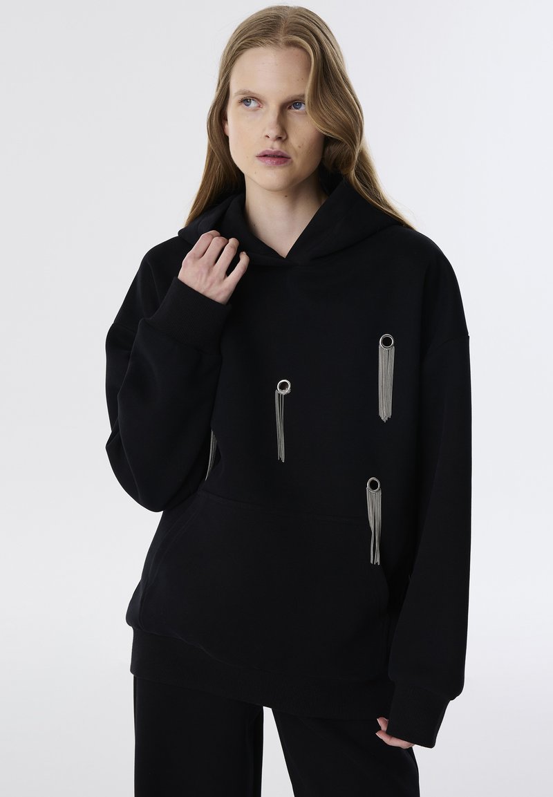 Sudadera negra con un gran bolsillo frontal, detalles en hardware plateado y borlas. Hecha de un material suave con un corte relajado.