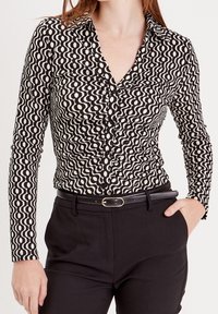 Chemise à manches longues noire et blanche avec un motif ondulé, un col à revers et des boutons. Associée à un pantalon noir ajusté et une ceinture.