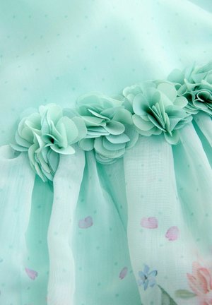 Lyseblåt gennemsigtigt stof med små polkaprikker, blomstermønster og en række lagdelte stofblomster langs en søm.