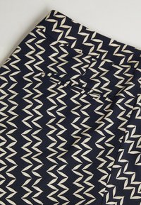 Granatowa spódnica z materiału z ivorową falistą kreską, z dopasowanym pasem i subtelnym detalem w postaci tylnej kieszeni. Gładka tekstura.