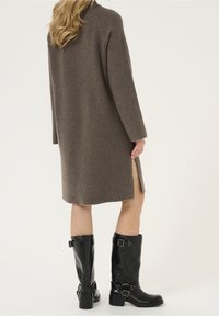 Brun ribbade stickade klänning med sidslitsar, kombinerad med svarta knähöga stövlar med spännen och blockklack.