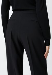 Crne krojene hlače s glatkom teksturom, koje imaju dva stražnja džepa i diskretne nabore za elegantan izgled.