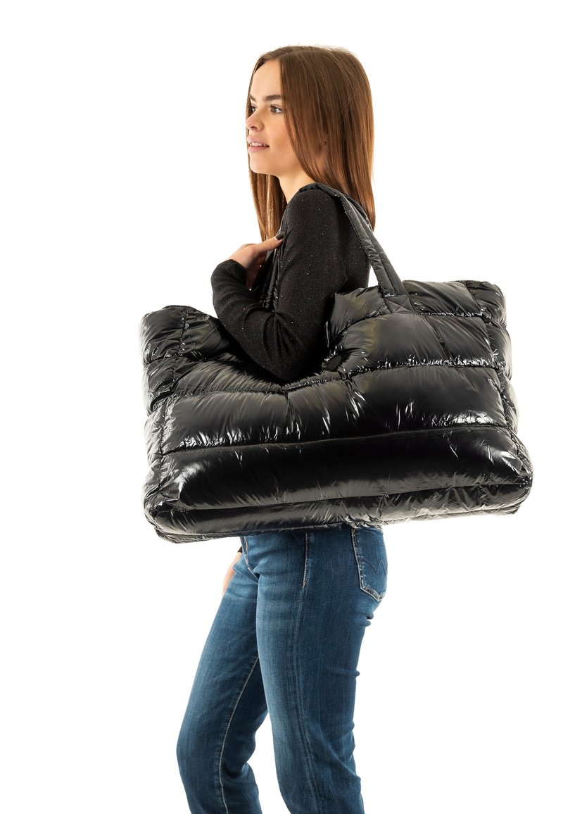 Borsa a tracolla nera con finitura lucida, caratterizzata da un design trapuntato, doppie maniglie e un interno grande e spazioso, portata sulla spalla.