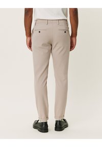 Beżowe spodnie o dopasowanym kroju, z dwoma tylnymi kieszeniami, czarnymi guzikami i podwiniętymi mankietami. Gładka tkanina z subtelnym połyskiem.