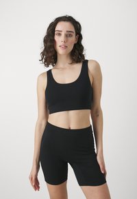 Fekete crop top és testhez simuló rövidnadrág rugalmas anyagból. Kerek nyakkivágással és varrás nélküli kialakítással a kényelem érdekében. Simaság jellemzi.