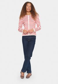Cardigan rayé rouge et blanc avec fermeture à boutons, associé à un jean bleu foncé et des ballerines à imprimé léopard. Tissu lisse, design ajusté.