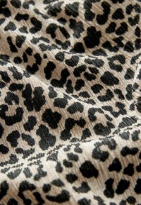 Tela beige con un patrón de print de leopardo negro, con un ribete texturizado. El diseño incluye diversas formas de manchas y remolinos.