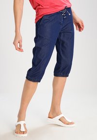 Námořnické denimové capri kalhoty s elastickým lemem a páskem na stažení, spárované s bílými žabkami. Hladká textura, ležérní design.