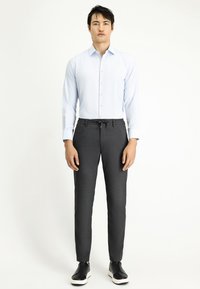 Lichtblauw overhemd met een subtiele patroon, gecombineerd met donkergrijze stretchbroek met een elastische tailleband en zwarte sneakers.